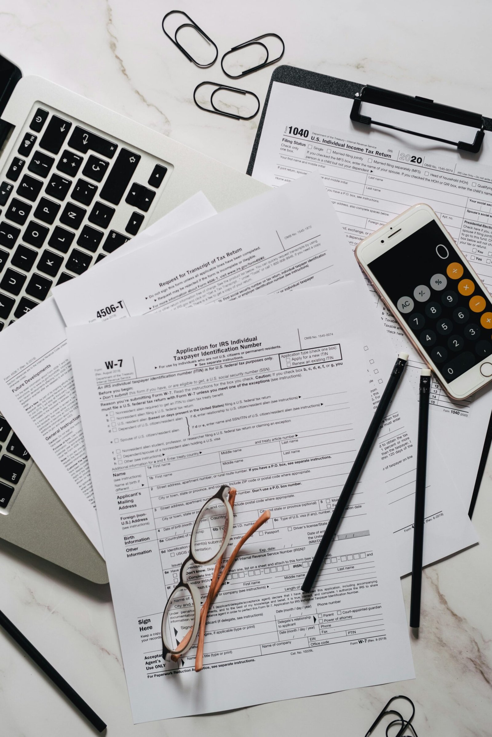 Arrangement of tax forms, calculator, and office supplies on a marble surface, top view.