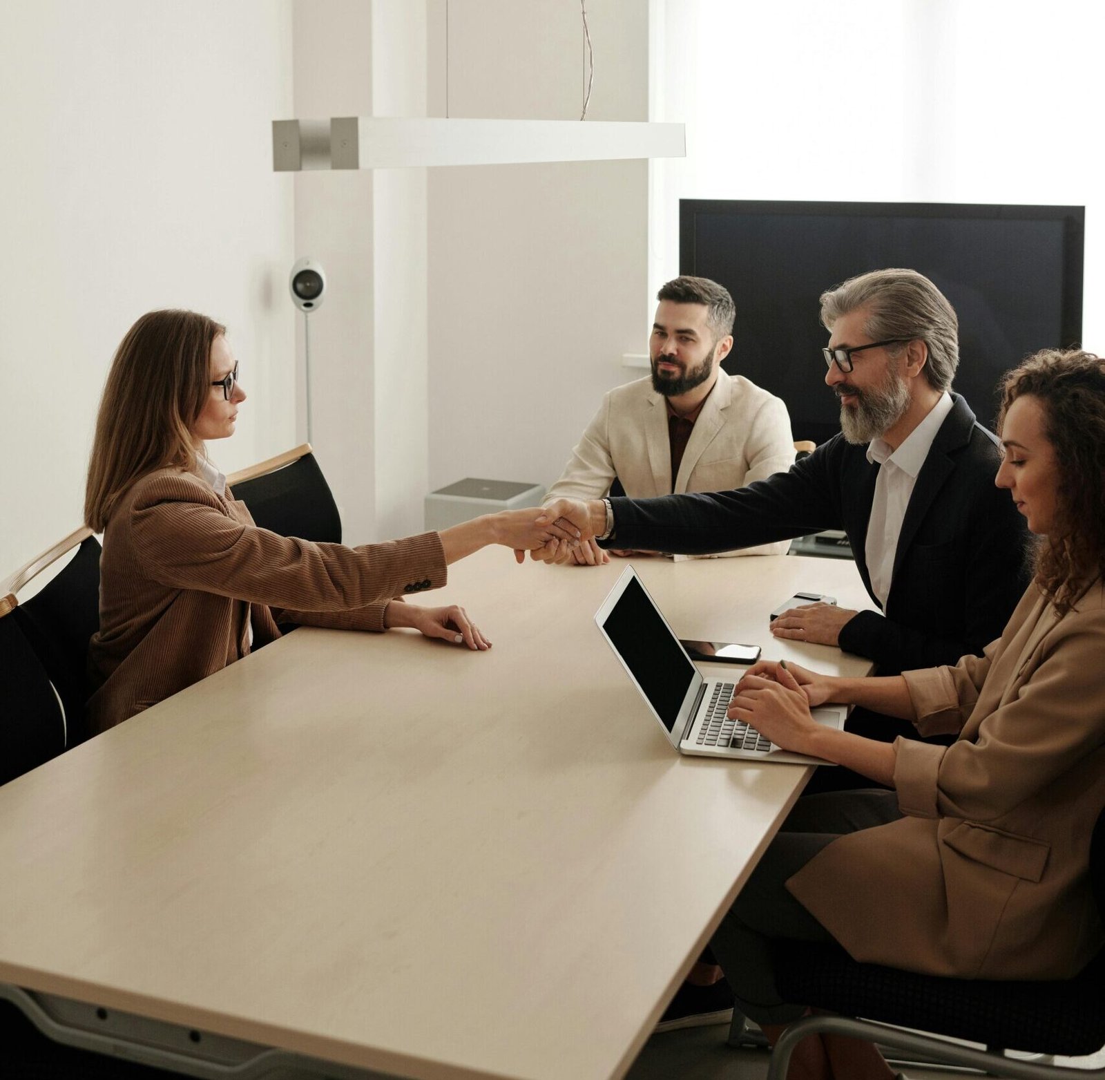 Business professionals engaging in a handshake across a conference table, signifying successful collaboration.
